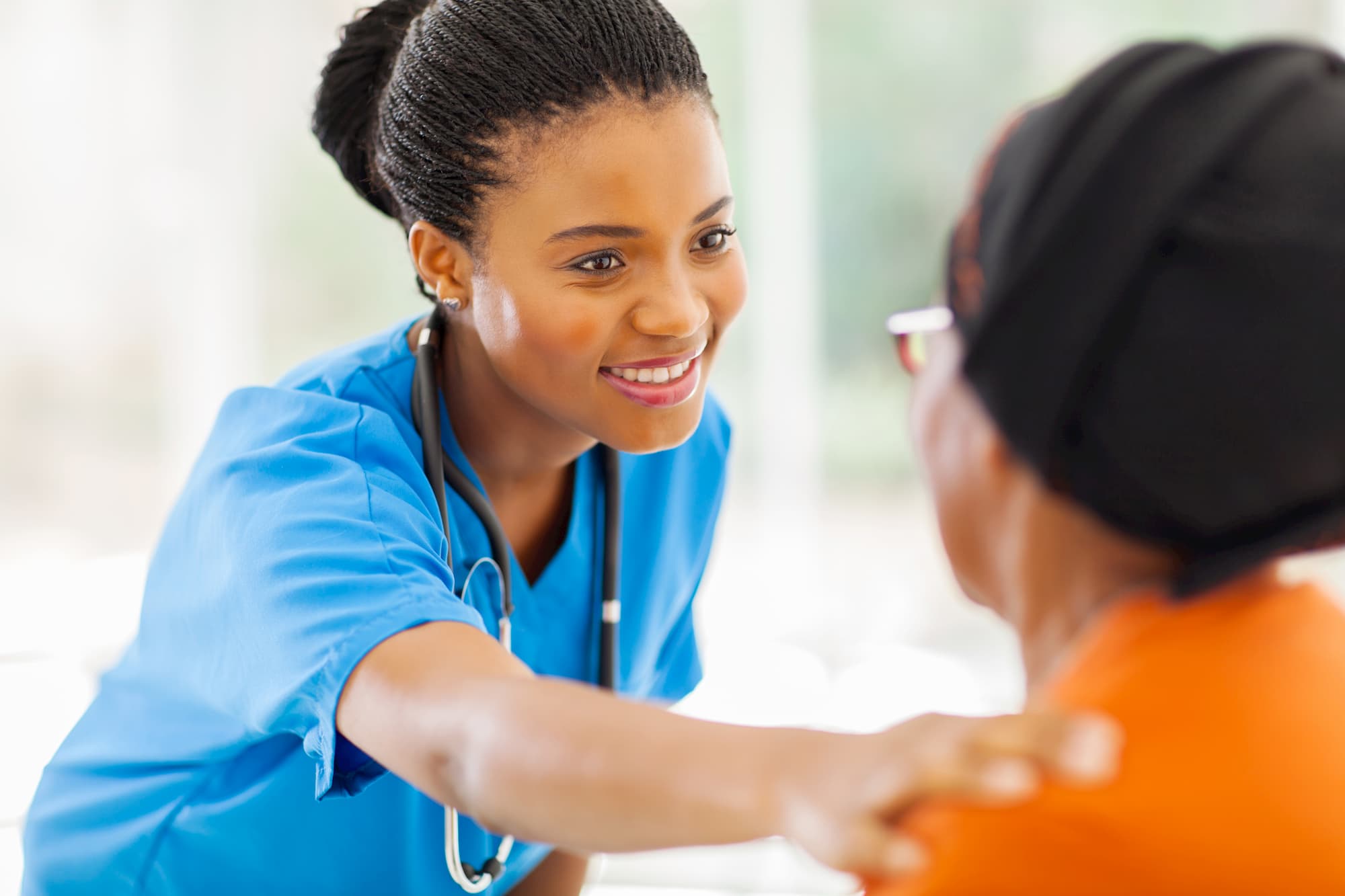 a doctor in scrubs smiling whilst placing her hand on a patients shoulder to try and console her