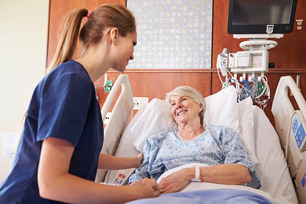 Nurse Talking To Senior Female Patient In Hospital Bed a patient sat up right in bed whilst smiling to a nurse who is checking on her